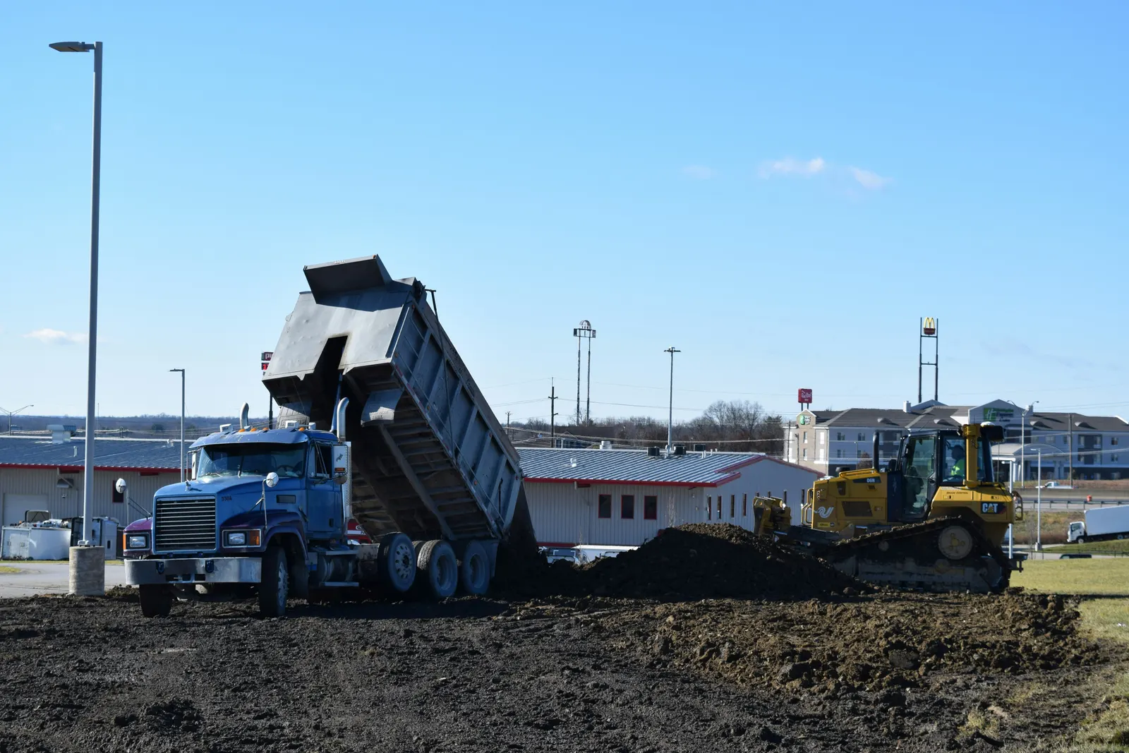 A tri-axle dump truck tipping fill while a dozer spreads it on a commercial site